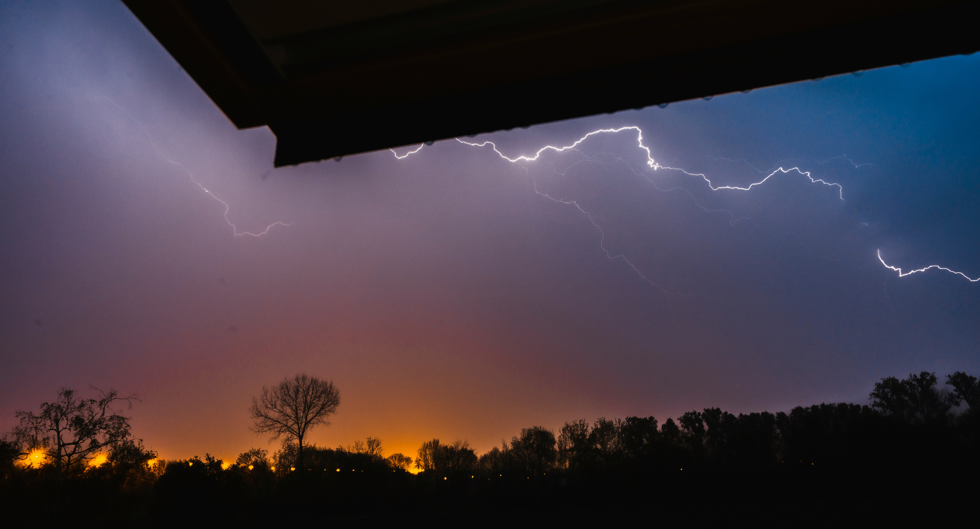 Lightning storm viewed from a roofline, lightning filling the upper frame with the roof edge in the lower third