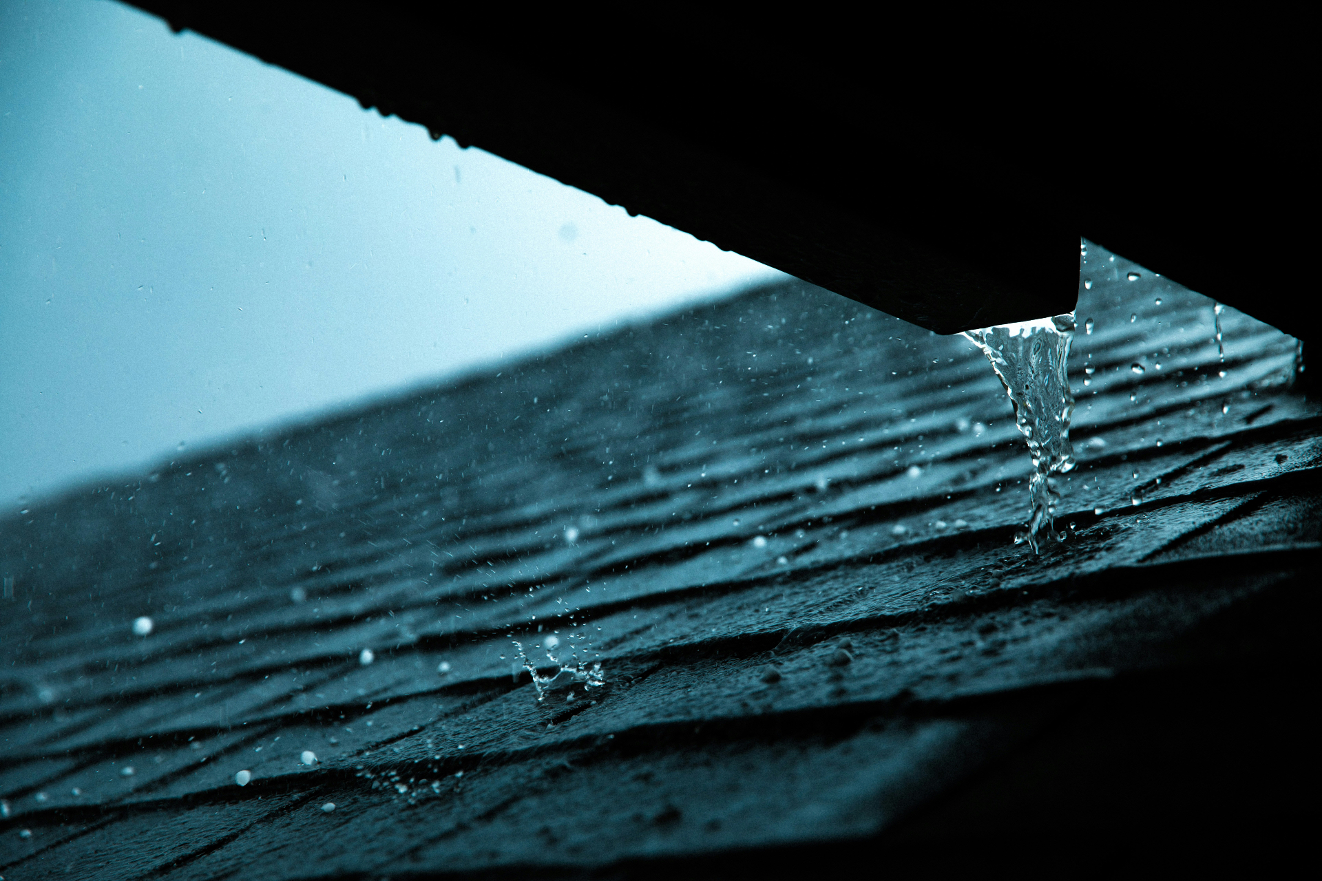 Rain pouring off dark asphalt roof shingles during a storm